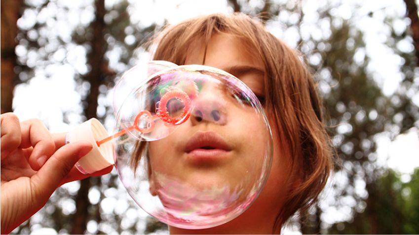 A girl blows a very large soap bubble.