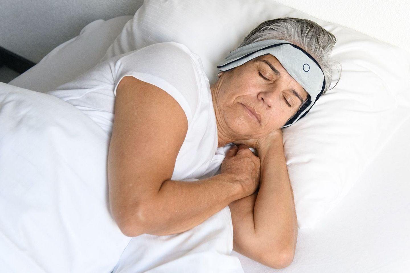 Eine Frau liegt schlafend im Bett, um den Kopf trägt sie ein Stirnband, das ihren Schlaf misst.