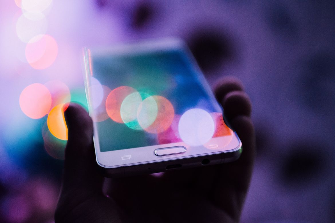 Eine Hand hält ein Mobiletelefon in die Luft und scheint dabei Daten zu empfangen und die Person Inhalte zu konsumieren.