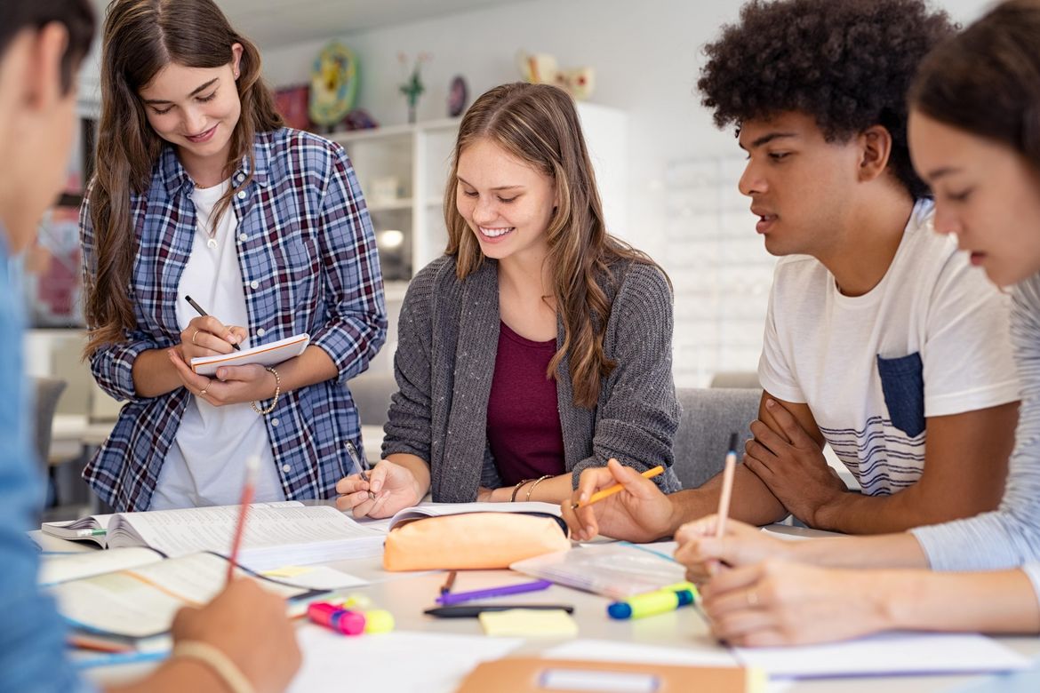 A group of young students sitting at a table and doing schoolwork together.