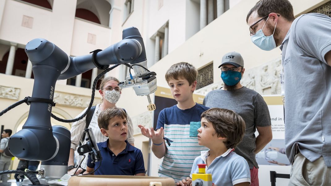 Kinder und Erwachsene schauen einen Roboterarm an.