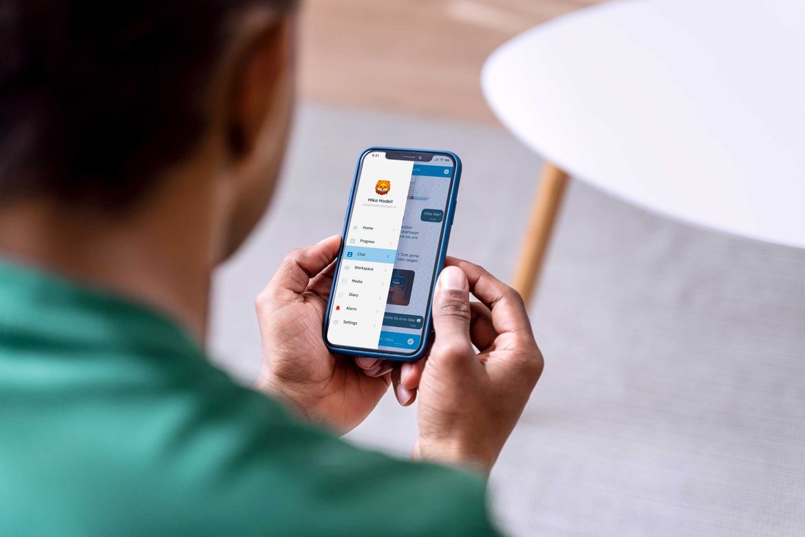 Ein Blick über die Schultern eines jungen Mannes, der ein Smartphone in den Händen hält, auf dessen Display die geöffnete App zu sehen ist.