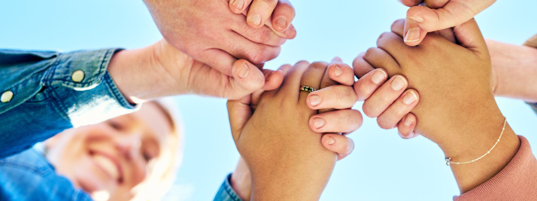 Fünf Menschen stehen eng im Kreis und halten sich fest an den Händen als Geste des Zusammenhalts.